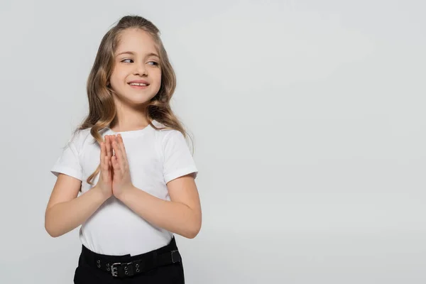 Menina positiva com as mãos orando sorrindo e olhando para longe isolado em cinza — Fotografia de Stock