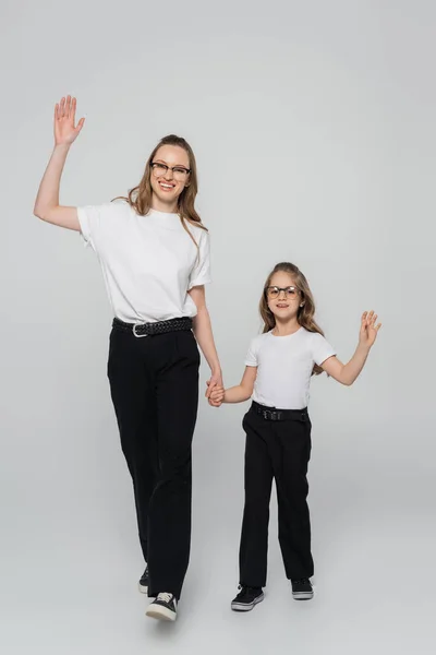 Visão de comprimento total de mãe e filha elegante sorrindo e acenando as mãos no fundo cinza — Fotografia de Stock