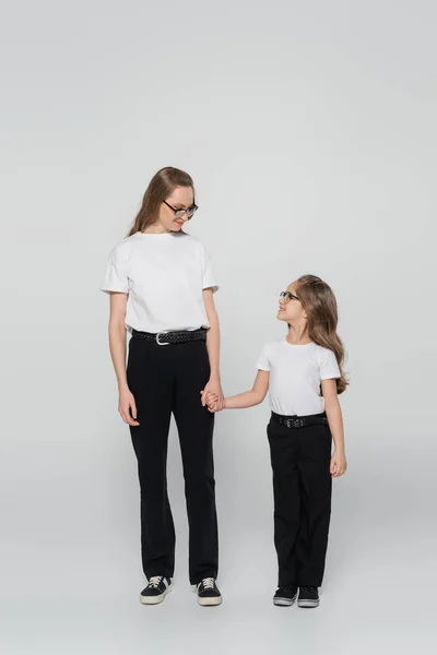 Full length view of mother and child holding hands and looking at each other on grey background — Stock Photo