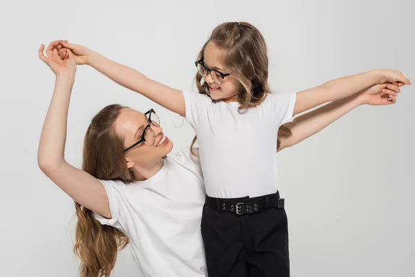 Mujer y niña en gafas de vista cogidas de la mano y mirándose aisladas en gris - foto de stock