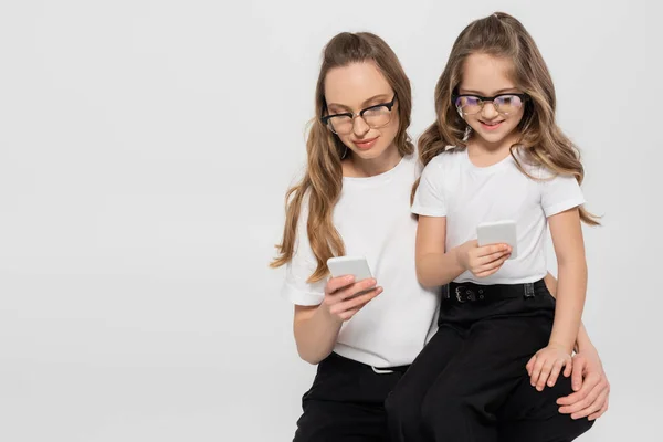 Woman and child in eyeglasses using smartphones isolated on grey — Stock Photo