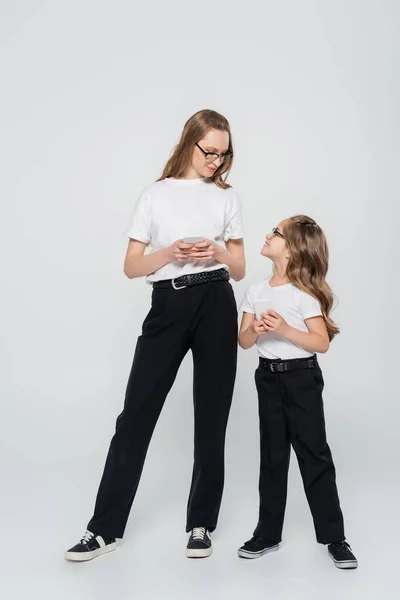 Femme et fille en noir et blanc vêtements tenant smartphones sur fond gris — Photo de stock