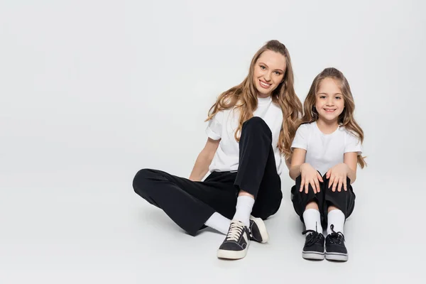 Joyful woman and girl in black and white clothes sitting on grey background — Stock Photo