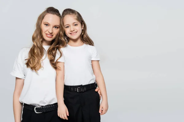 Mujer elegante con hija sonriendo a la cámara aislada en gris - foto de stock