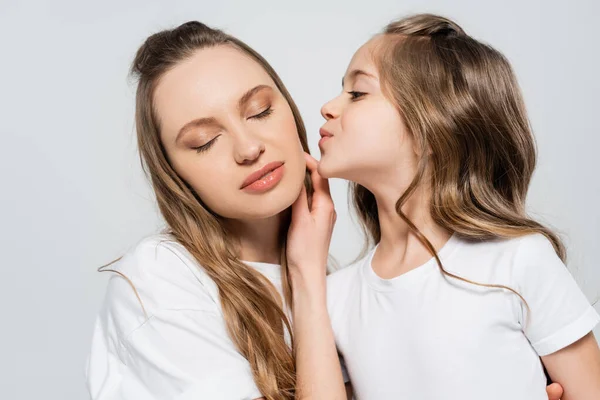 Mulher com os olhos fechados perto da filha beijando-a isolada no cinza — Fotografia de Stock