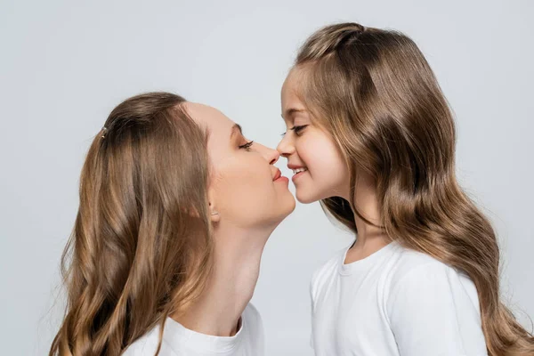 Vista lateral de mujer e hija con el pelo largo mirándose cara a cara aisladas en gris - foto de stock