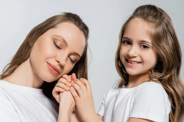 Feliz chica y mujer con los ojos cerrados tomados de las manos aislados en gris - foto de stock