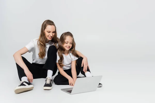 Happy mother and daughter watching movie on laptop on grey background — Stock Photo