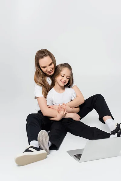 Feliz madre e hija abrazando y viendo la película en gris - foto de stock