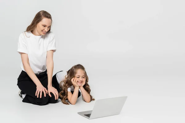 Alegre madre e hija viendo la película en el ordenador portátil sobre fondo gris - foto de stock