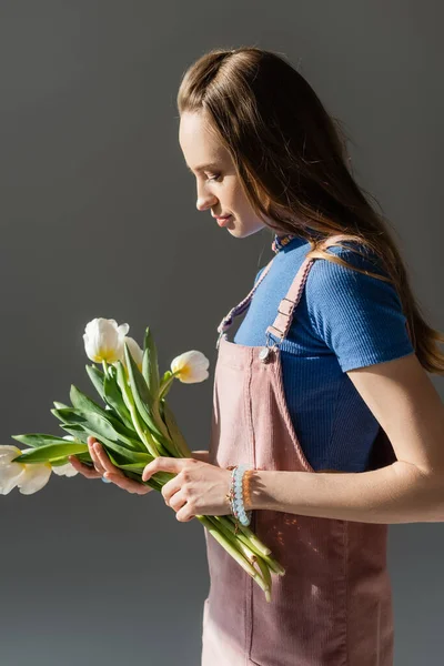 Vue latérale de la femme tenant des tulipes en fleurs isolées sur gris — Photo de stock