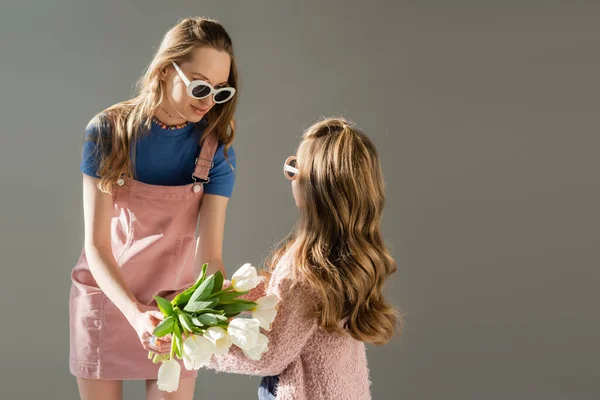 Mutter mit Sonnenbrille erhält Blumen von Tochter isoliert auf grau — Stockfoto