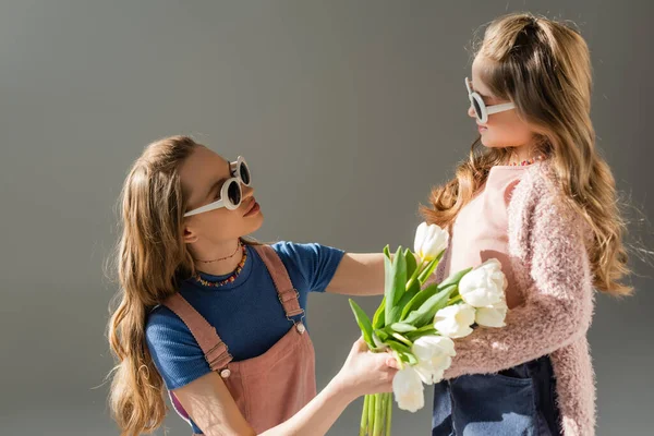 Mère en lunettes de soleil recevant des fleurs de fille heureuse isolée sur gris — Photo de stock