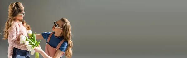 Mutter mit Sonnenbrille erhält Blumen von glücklicher Tochter isoliert auf grauem Banner — Stockfoto