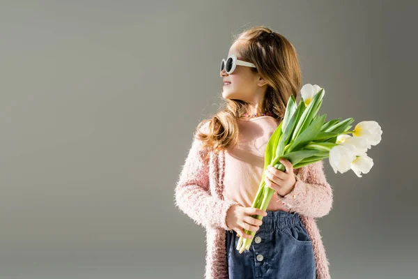 Niño feliz en gafas de sol sosteniendo flores aisladas en gris - foto de stock