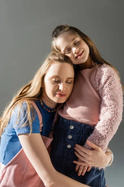 Cheerful mother and daughter with closed eyes hugging isolated on grey — Stock Photo