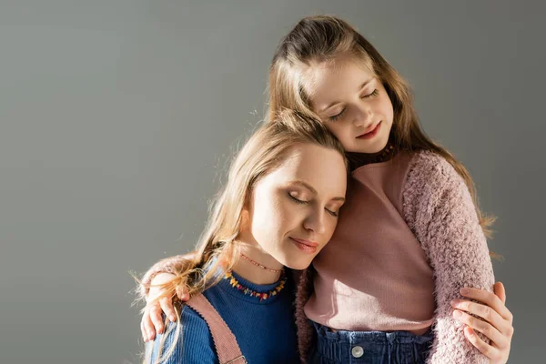 Pleased mother and daughter with closed eyes hugging isolated on grey — Stock Photo