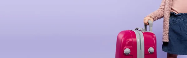 Vue recadrée de l'enfant tenant poignée de bagage isolé sur violet, bannière — Photo de stock