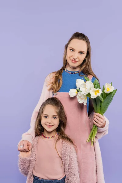 Femme heureuse tenant des tulipes près de fille isolé sur violet — Photo de stock