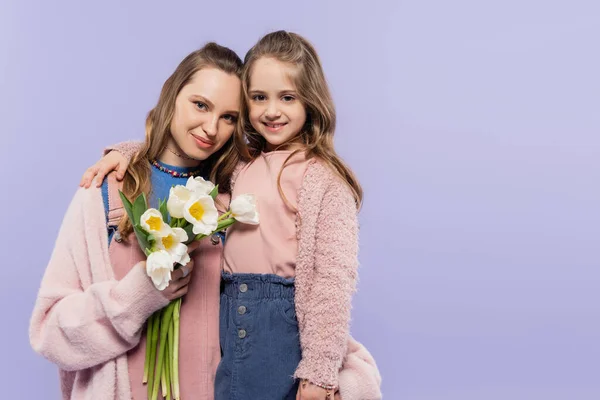 Mulher feliz segurando tulipas perto de sorrir filha isolada em roxo — Fotografia de Stock