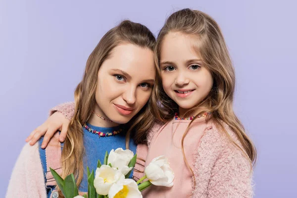 Woman holding tulips near smiling daughter isolated on purple — Stock Photo