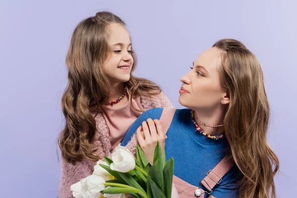 Lächelnde Frau mit Tulpen und Blick auf glückliche Tochter isoliert auf lila — Stockfoto