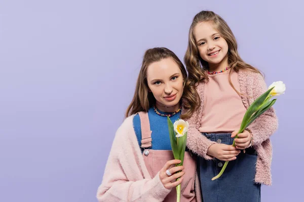 Madre e hija complacidas sosteniendo tulipanes aislados en púrpura - foto de stock
