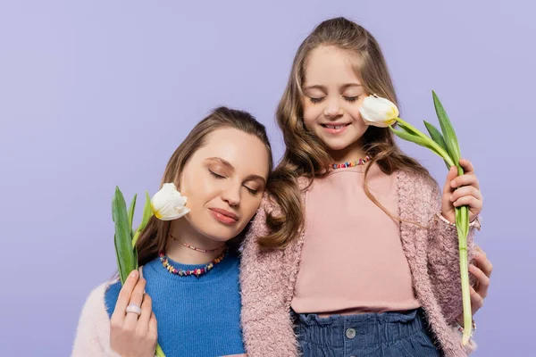 Complacidos madre e hija con los ojos cerrados sosteniendo tulipanes aislados en púrpura — Stock Photo