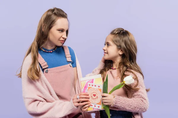 Мати тримає вітальні листівки і дивиться на щасливу дочку з тюльпаном ізольовано на фіолетовому, концепція Дня матері — стокове фото