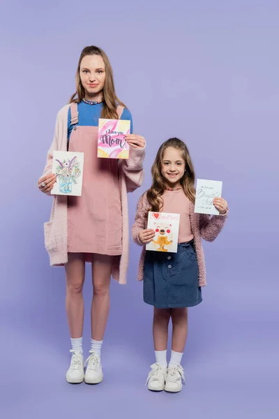 Comprimento total de mãe e filha feliz segurando cartões no roxo, conceito dia das mães — Fotografia de Stock