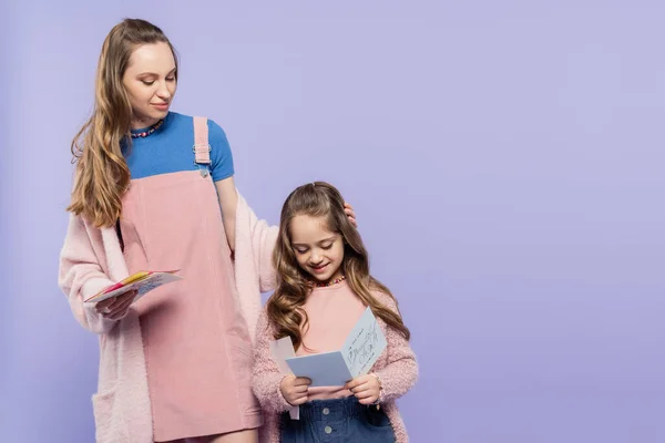 Cheerful kid reading greeting card to mother isolated on purple — Stock Photo