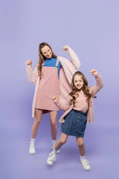 Full length of happy mother in pink overall dress dancing with joyful girl on purple — Stock Photo