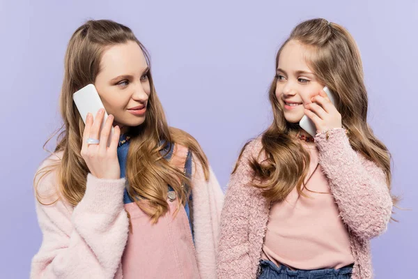 Felice madre e figlia che parlano sui telefoni cellulari isolati su viola — Foto stock