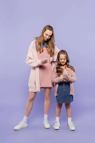 Longitud completa de la madre y la hija usando gadgets en púrpura - foto de stock