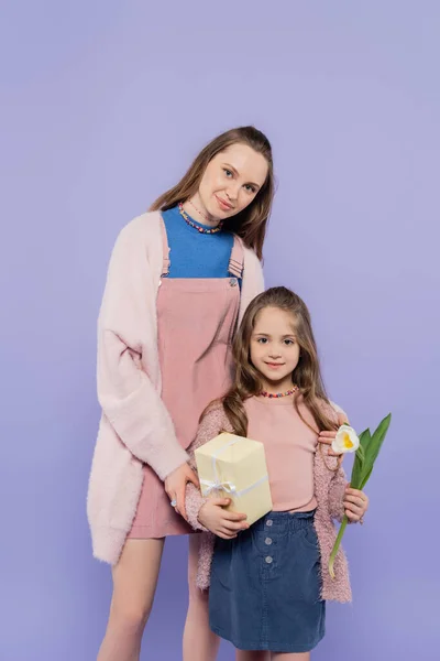 Glückliches Mädchen hält Geschenkbox und Tulpe in der Nähe Mutter isoliert auf lila — Stockfoto