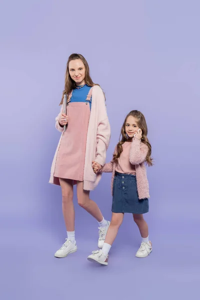 Full length of mother holding hands with child talking on smartphone on purple — Stock Photo