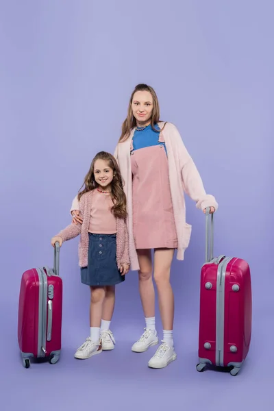 Comprimento total de mãe feliz e criança de pé perto da bagagem em roxo — Fotografia de Stock