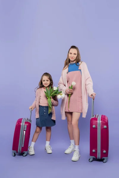 Повна довжина щасливої матері і дитини, що тримає квіти біля багажу на фіолетовому — стокове фото