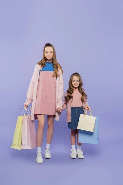 Full length of pleased mother and daughter holding shopping bags on purple — Stock Photo