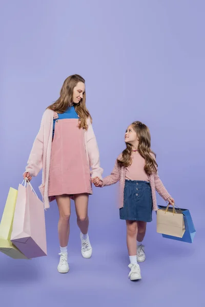 Longitud completa de la madre y la hija sosteniendo bolsas de compras mientras camina sobre púrpura - foto de stock