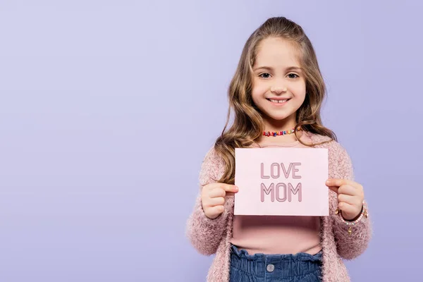 Happy kid holding greeting card with love mom lettering isolated on purple — Stock Photo