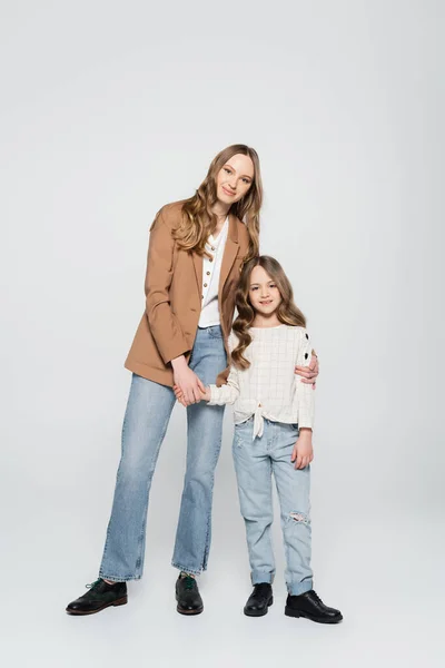 Full length of positive mother and smiling daughter hugging on grey — Stock Photo