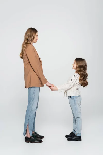 Side view of smiling mother and daughter holding hands on grey — Stock Photo