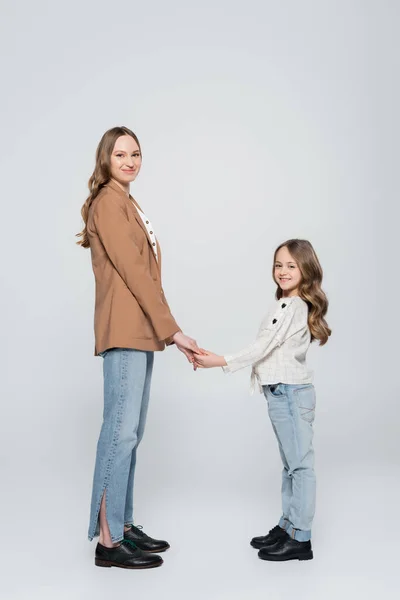 Full length of positive mother and daughter holding hands on grey — Stock Photo
