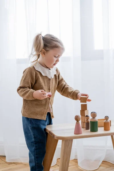 Kleines Mädchen spielt zu Hause mit Holzwürfeln und Figuren — Stockfoto