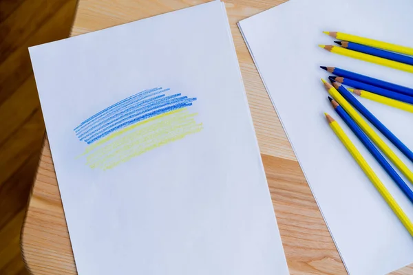 Top view of white paper with blue and yellow strokes near color pencils on wooden table — Stock Photo