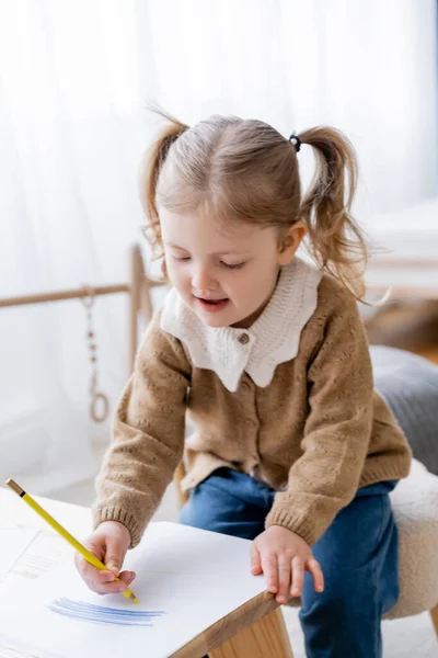 Concentrated girl drawing with yellow pencil on paper with blue strokes — Stock Photo