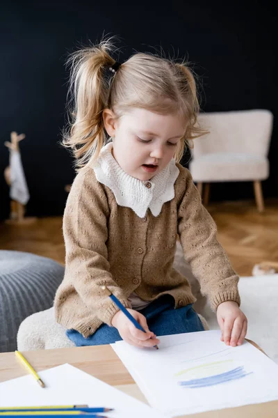 Девушка рисует синими и желтыми карандашами, сидя дома — стоковое фото
