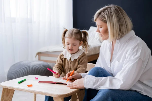 Blonde Frau und Mädchen mit Pferdeschwanz zeichnen mit bunten Filzstiften zu Hause — Stockfoto