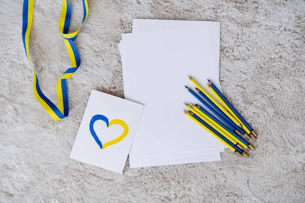 Vista dall'alto di matite a colori, nastro e carta con cuore blu e giallo su tappeto grigio soffice — Foto stock